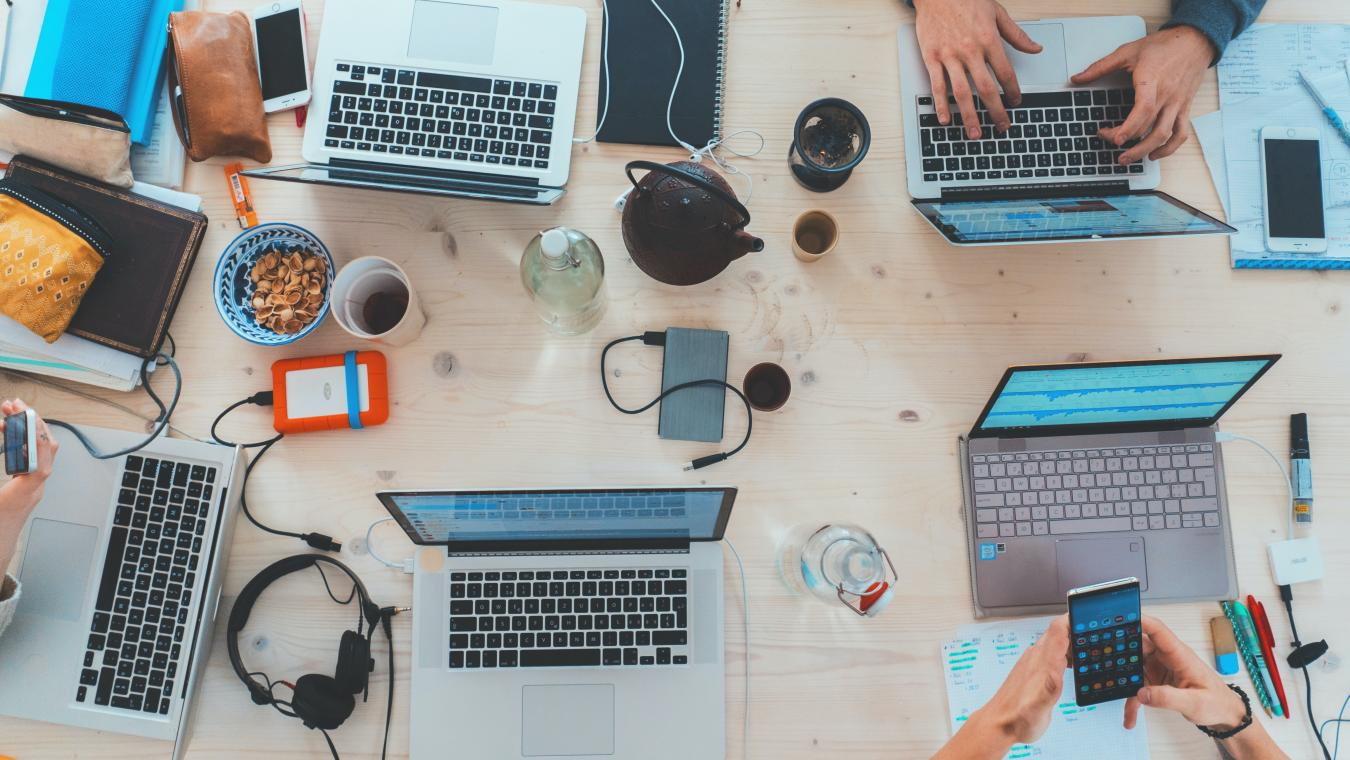 A top-down view of people working together at a table, with only their hands, laptops and handheld devices visible